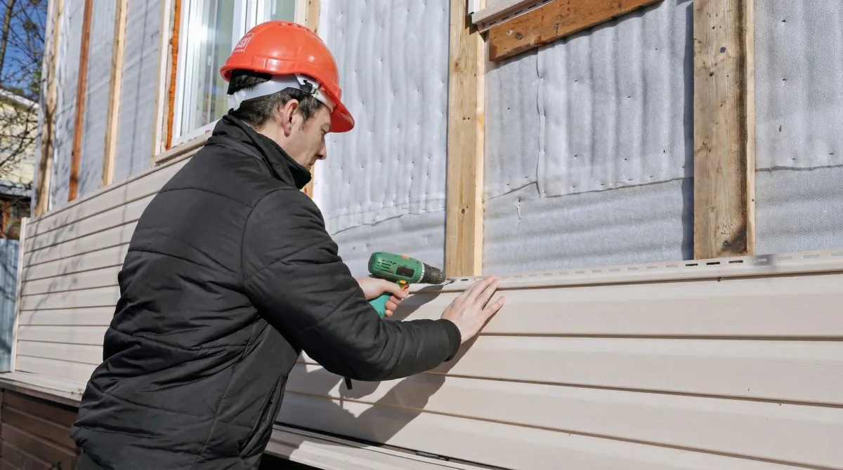Siding replacement professional using a power drill to install new tan vinyl siding on a home exterior in El Paso, TX